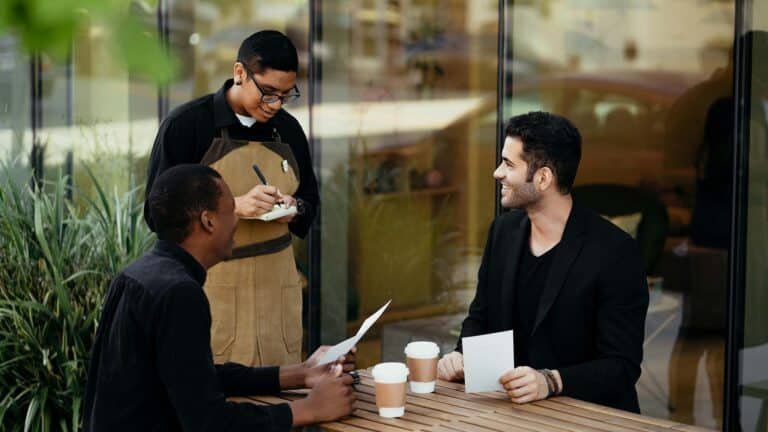 Two guests sitting in a restaurant talking to a waiter.